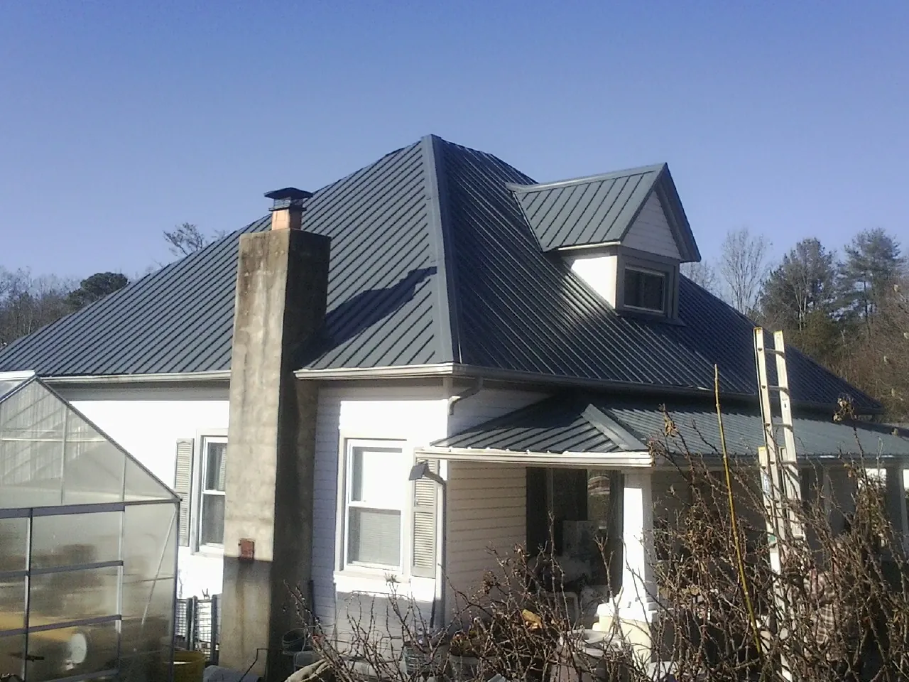Dark blue standing seam metal roof on a white farmhouse with dormer in Reubens