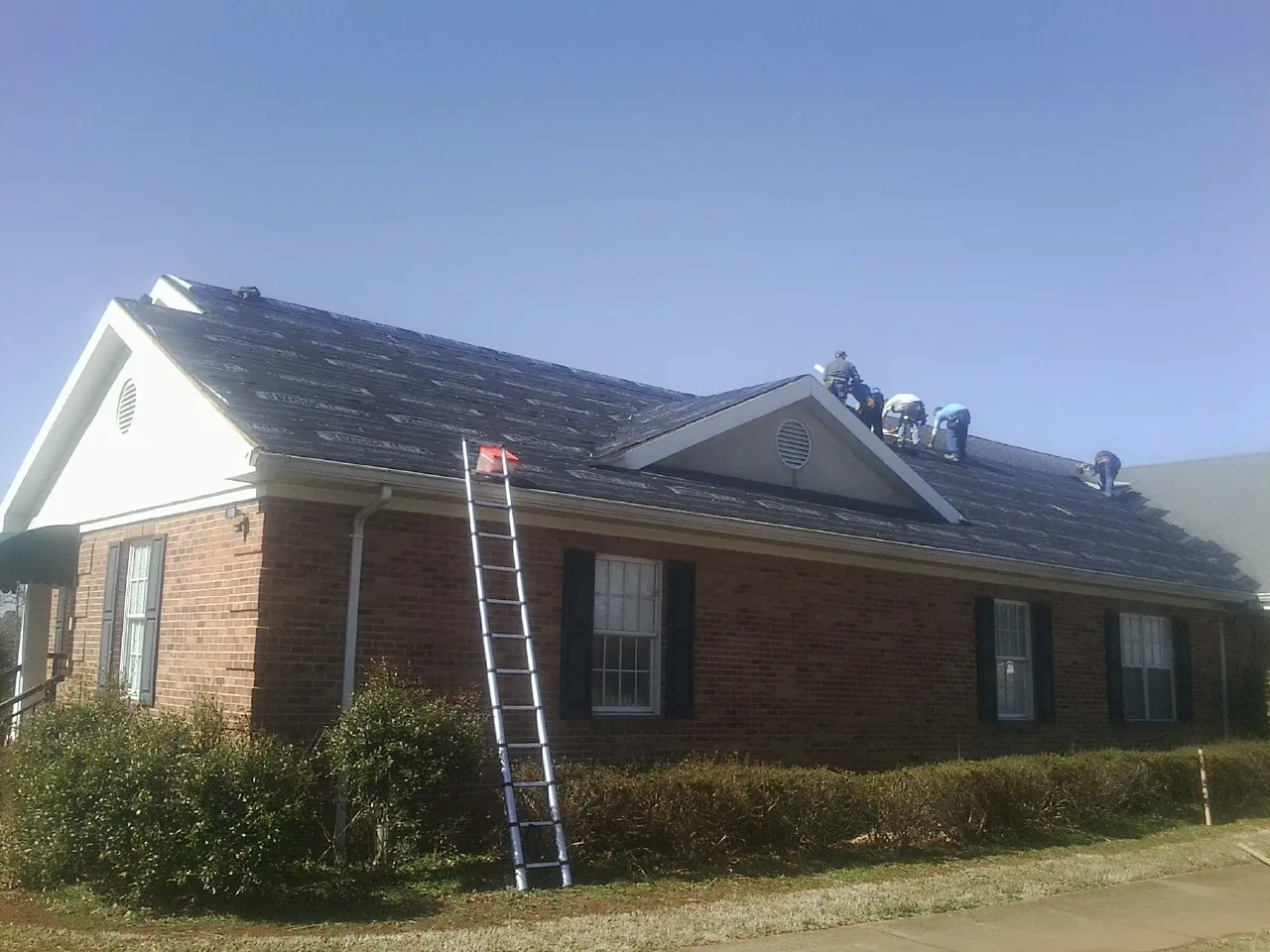 Crew tearing shingles off a brick ranch roof with a ladder set — Metal Roof Repair work by our crew in Reubens