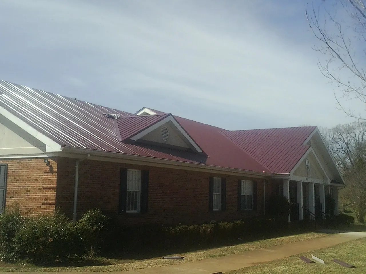 Red metal roof with gabled entries on a long brick building, from a Hail Damage Roof Repair job in Reubens