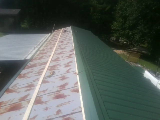Old rusted panels beside newly installed green metal roofing — Wind Damage Roof Repair by Roofing Brothers in Reubens