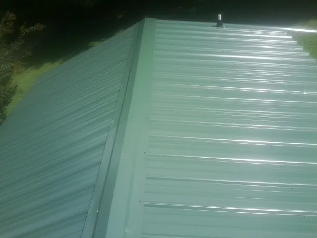 New green metal panels meeting at the ridge of a roof — Flat Roof Repair work by our crew in Reubens