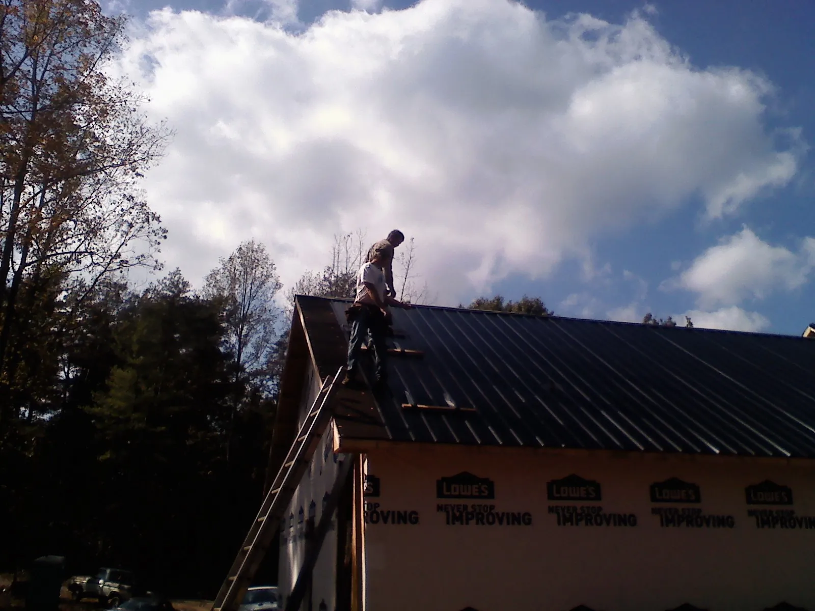 Roofer fastening dark metal panels high against a cloudy sky, from a Roof Inspection job in Reubens