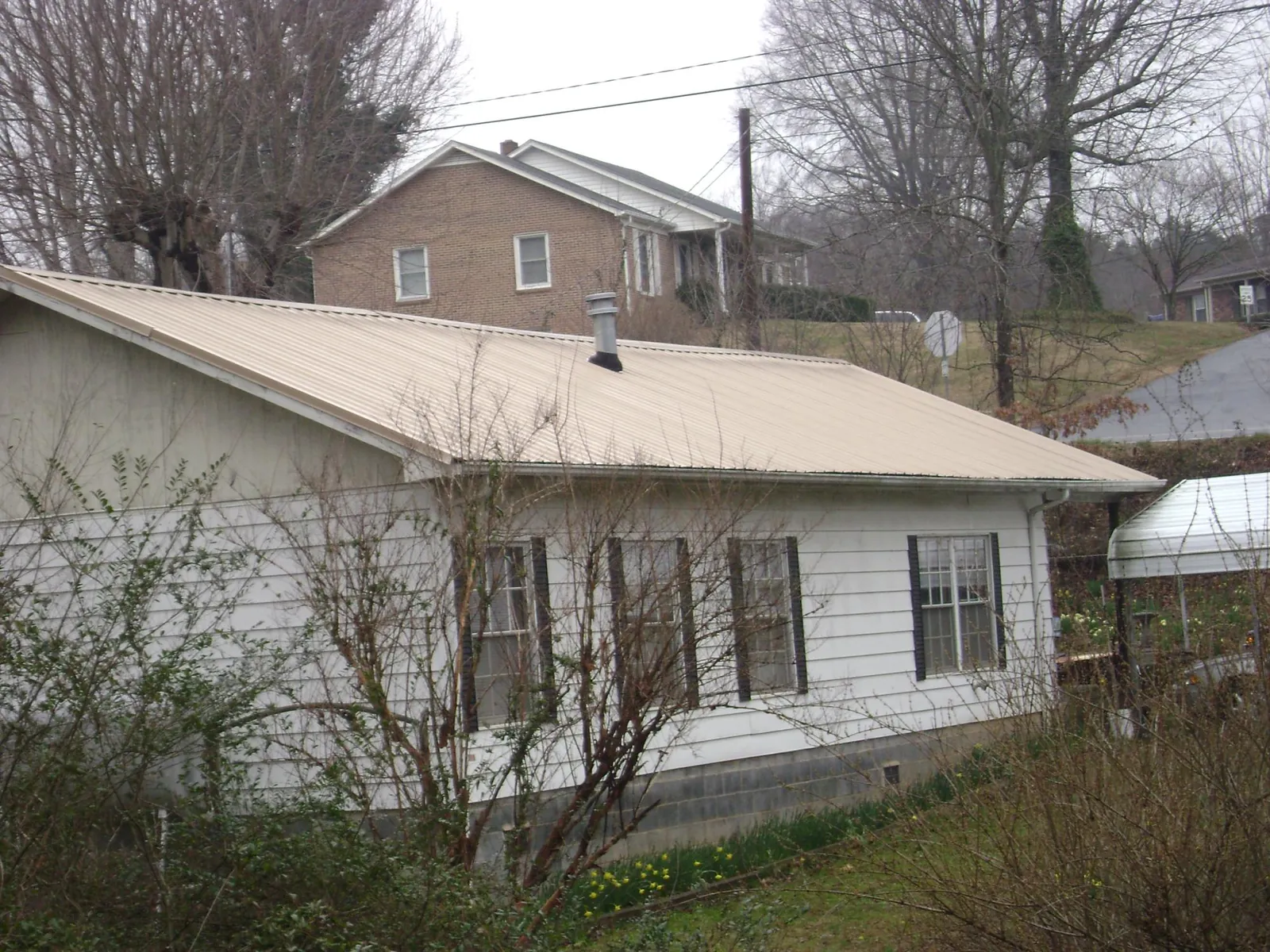 Tan metal roof on a white sided house set into a hillside — Commercial Roofing by Roofing Brothers in Reubens